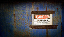 Sign warns workers of asbestos danger and promotes protective clothing.